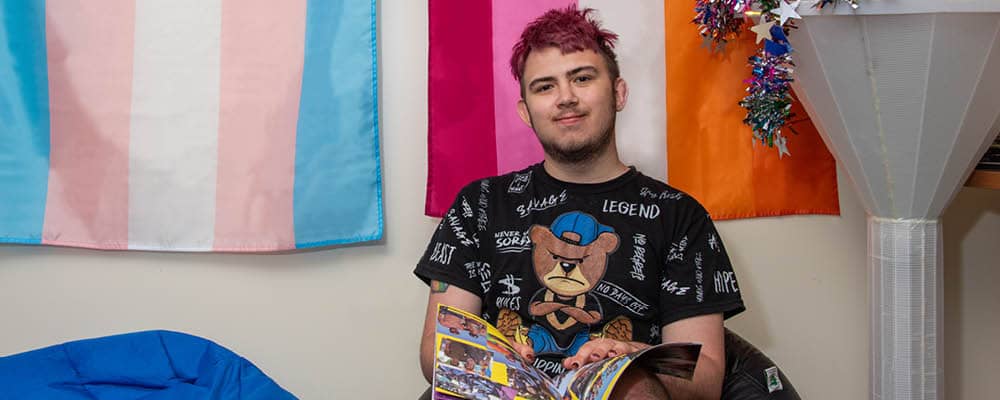 An FLCC student sits in front of a row of pride flags hanging on the wall.